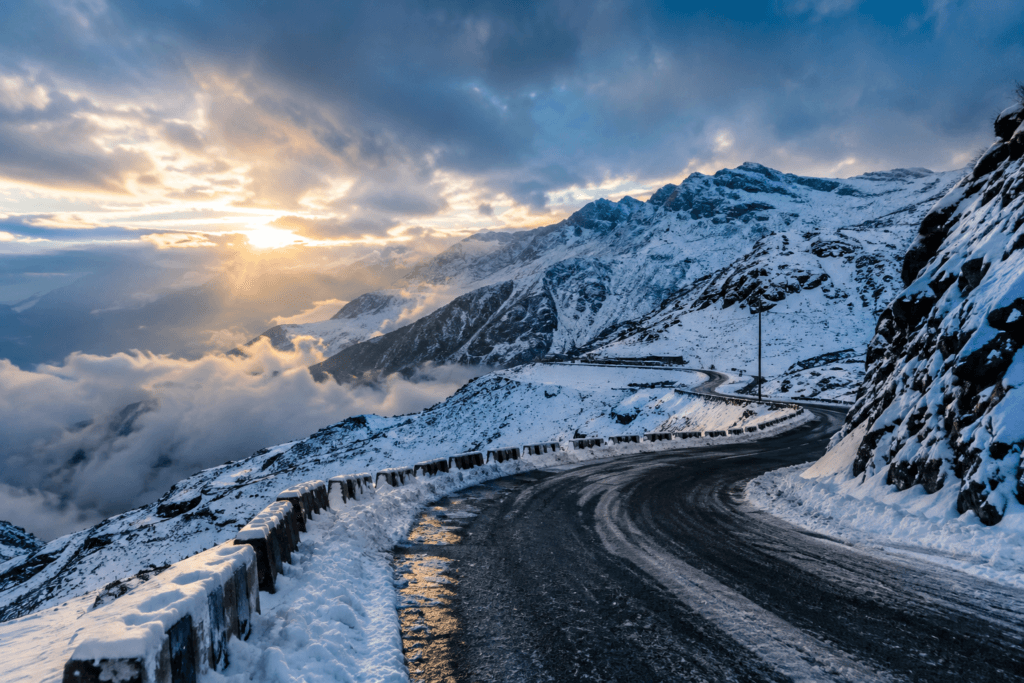 Snow-covered Sela Pass mountain road winding through dramatic Himalayan peaks at sunset